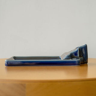 Side view of navy ceramic incense holder tray on a ledge surface.