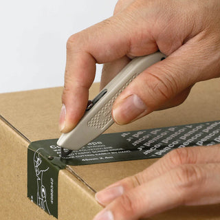 Ivory pocket utility knife in hand, cutting cardboard box with blade extended