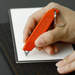 Pocket utility knife in orange held in hand with lanyard chain