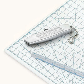Silver pocket utility knife with keychain lanyard on cutting mat