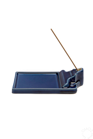 Navy ceramic incense holder with raised side supports and incense stick inserted.