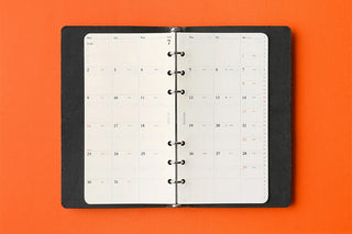 Open monthly schedule refill booklet with white calendar pages and black binding