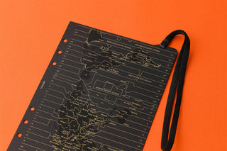 A5 notebook corner with orange dots and circuit-map print, black strap visible