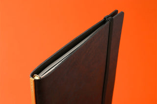 A5 notebook edge view with dark cover, gold spine label, and band closure