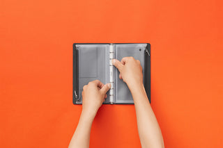 Bible-size fastener case opened, hands adjusting the clasp on gray pocket panels