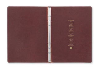 Open red-brown leather binder with metal ring and text block on inner cover