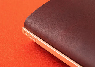 Red-brown leather binder cover edge with engraved logo strip along the spine