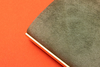 Close-up of green leather mini binder cover edge with textured grain and cream spine lining