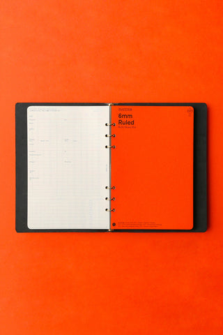 Black A5 6-ring binder open, ruled pages and ring mechanism visible.