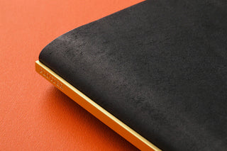 Black leather binder close-up: narrow side edge with gold-tone trim