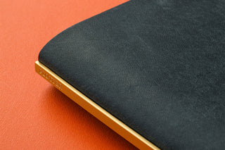 Navy leather binder close-up showing gold-edged spine and cover seam.