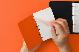 Hand holding white refill memo pad sheets over a ring-binder, perforated edges