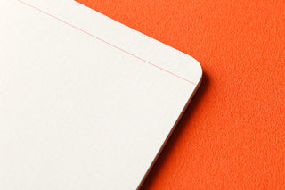 Corner of a white memo pad sheet with faint 2mm grid and a thin red guide line