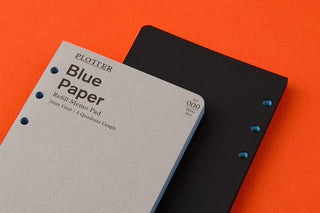 Blue memo pad refill beside black pad, punched holes, PLOTTER label