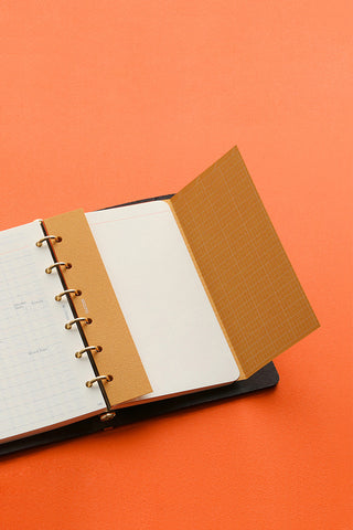 Mini ring binder planner with orange cover pages and white inserts on a base
