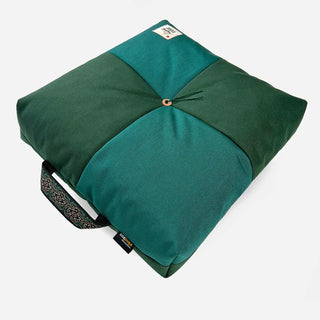 Folded teal and green outdoor cushion with logo patch and curved button clasp
