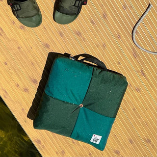 Green folded outdoor cushion with center button and fabric carry strap loop