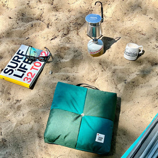 Green folded outdoor cushion with center button and small logo patch
