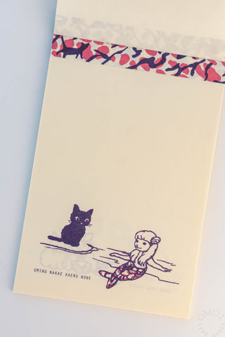 Beige cat memo pad with pink patterned top strip and cat with a small character on a board