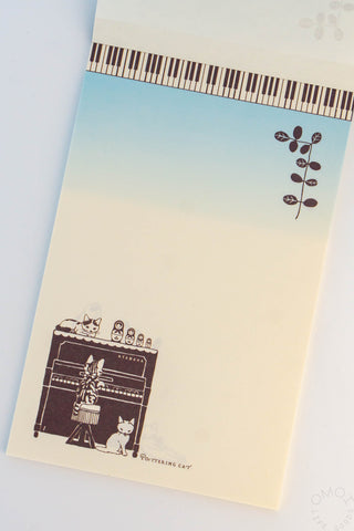 Cat and piano letter pad with piano-key strip, branch motif, and cats surrounding piano