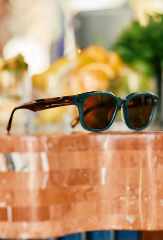 Close-up of teal sunglasses with dark brown lenses on an outdoor ledge