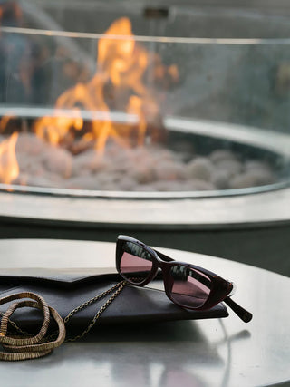 Iwa sunglasses lying down with dark cherry frames and rose tinted lenses, with chain