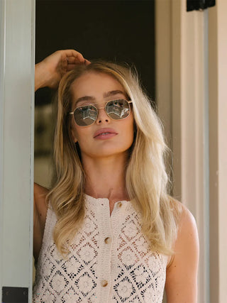 Woman wearing silver sunglasses with brown tinted lenses and thin gold-toned arms.