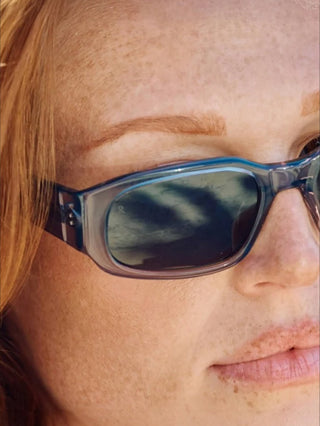 Close-up of dark smoke sunglasses with blue-gray translucent frame and curved lens