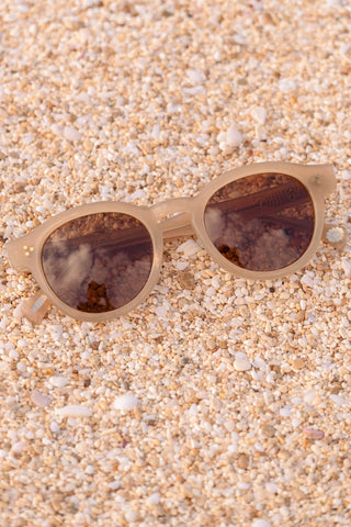Round sunglasses with light beige frame and brown lenses on sand