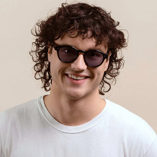 RAEN round sunglasses on person, black frame with dark blue lenses