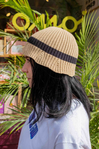 Beige knit beanie with wide black stripe, worn with long hair