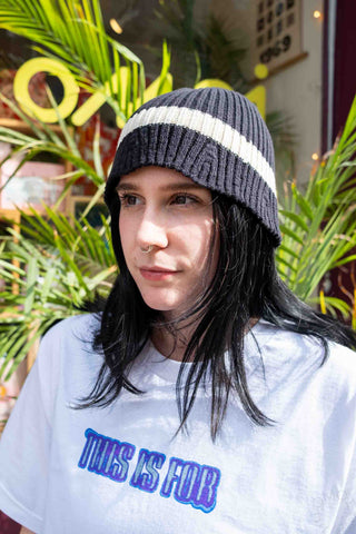 Dark gray knit beanie with wide cream stripe, worn with long hair