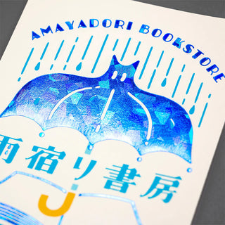 Close-up foil postcard with blue umbrella and wave lines; AMAYADORI BOOKSTORE title at top