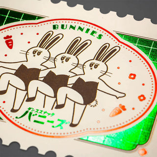 Close-up stamp-shaped foil postcard showing three bunnies in an oval