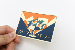 Hand holding retro fruit parlor sticker card with grapes, checkerboard, and blue border