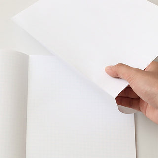 Pocket grid notebook pages with white grid paper; hand lifts a sheet corner
