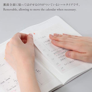 Hands adjusting removable weekly calendar stickers on beige planner pages