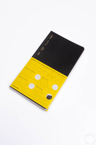 Black slim notebook with yellow cover label band, slightly angled