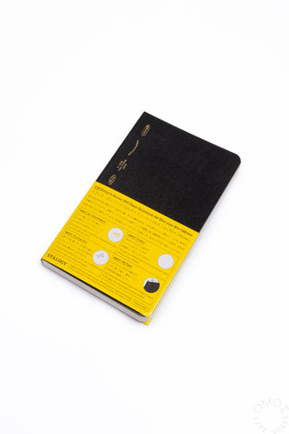 Black slim notebook with yellow label band on the cover, angled view