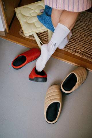 Beige quilted slippers with black interior, placed near a red pair