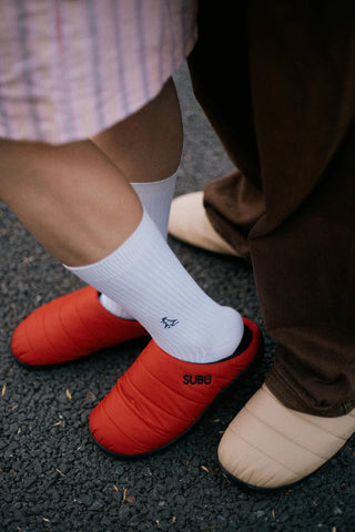 Beige slip-on slippers with black lining and white socks, paired with red slippers