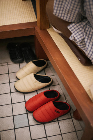 Pair of beige quilted slippers with black trim, shown on a tiled floor