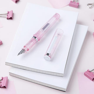 Pink glassy fountain pen with clear cap on open notebook
