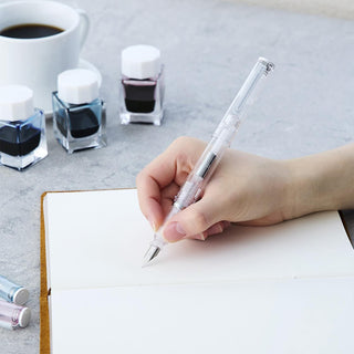 Pink glassy fountain pen held in hand, nib over white writing paper