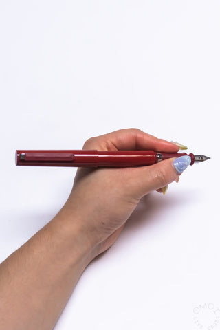 Red fountain pen held in hand with nib exposed and clip details