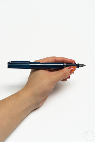 Translucent dark blue fountain pen held in hand with nib exposed