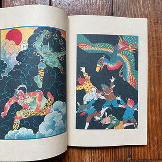 Open art book showing two colorful mythic illustrations on separate pages