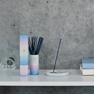 Incense sticks in gradient blue and pink holder on a table with white ash tray