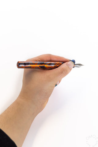 Orange smoke marbled fountain pen held by hand, metal nib visible