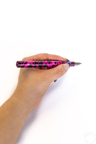 Hand holding pink fountain pen with black speckle pattern and exposed metal nib